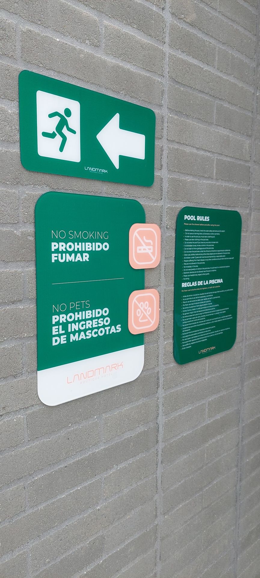 Hotel signs with no smoking, no pets, and pool rules on a brick wall.