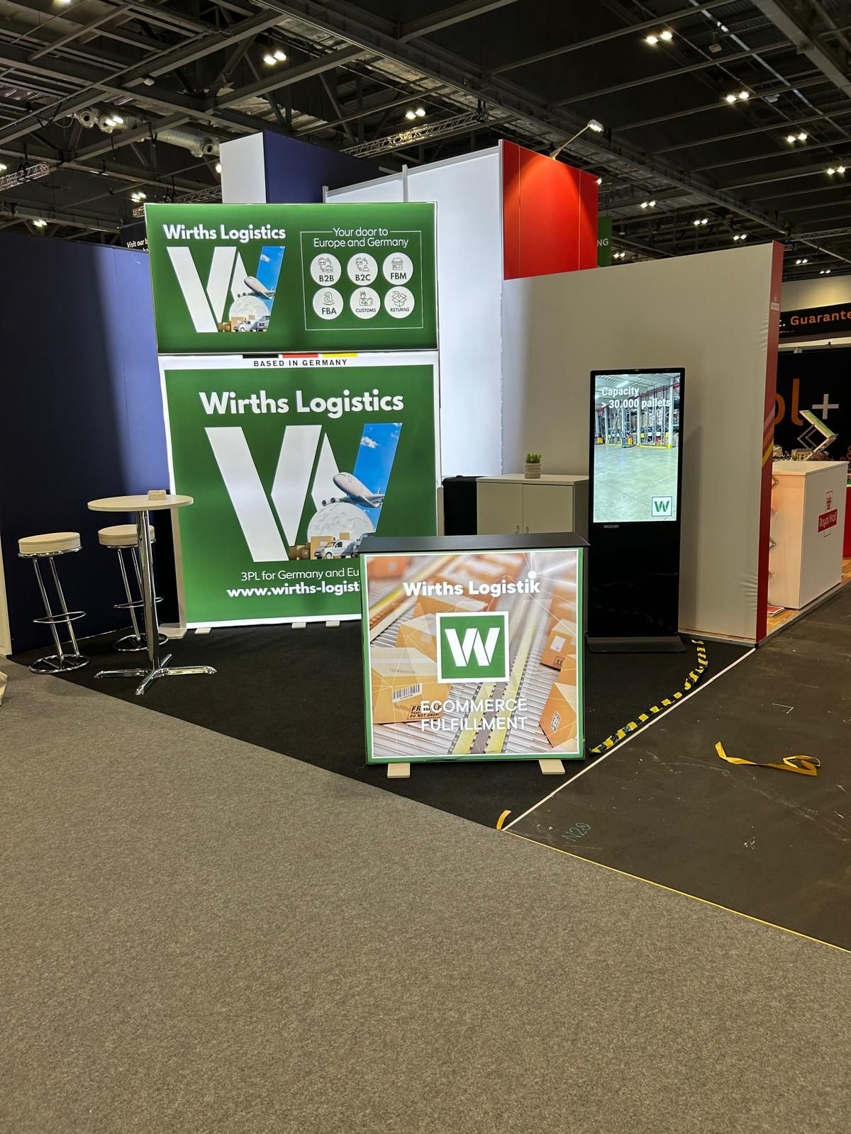 Exhibition booth for Wirths Logistics with display screens and informational banners highlighting ecommerce fulfillment services.